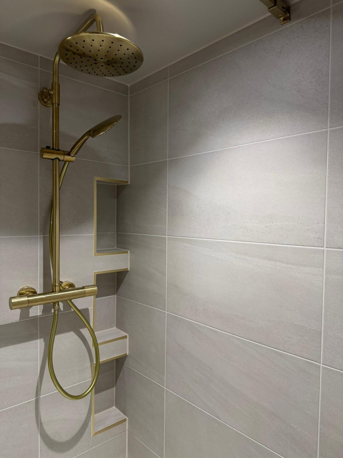 Walk-in shower installation with brushed brass fittings and neutral bathroom tiles